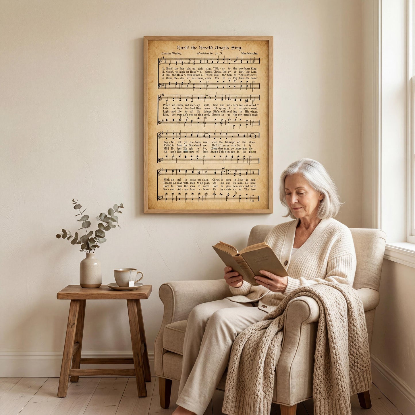 An elderly woman is sitting in a chair, reading a book, with a framed sheet music display hanging on the wall behind her.