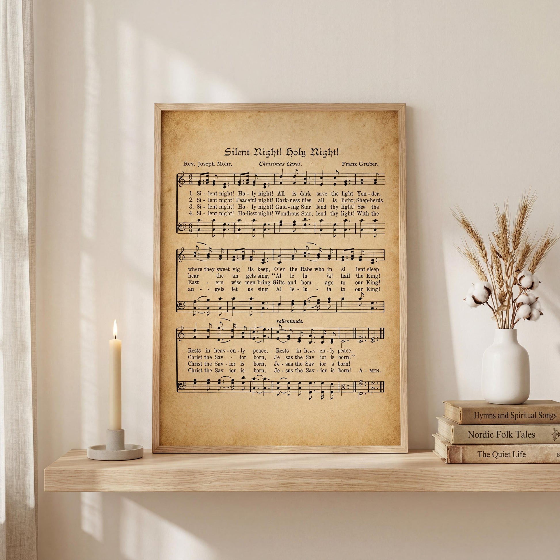 a framed sheet music print of a hymn titled "Silent Night! Holy Night!" displayed on a shelf next to a lit candle and some books.