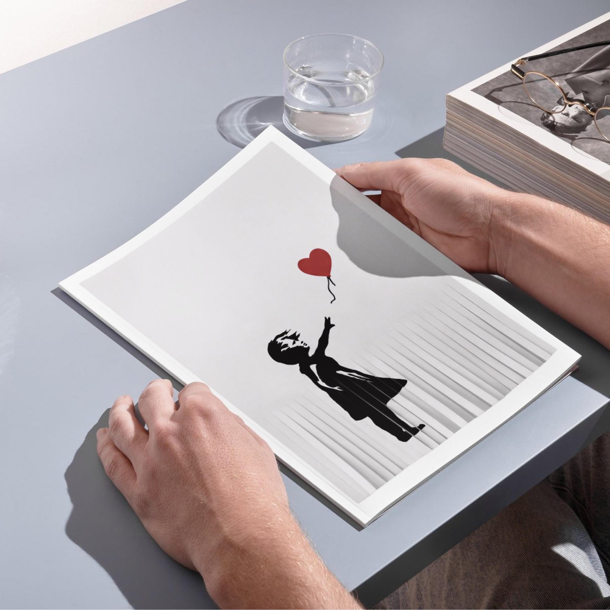 A person's hands are holding a book with a black and white illustration of a person holding a red heart-shaped balloon.