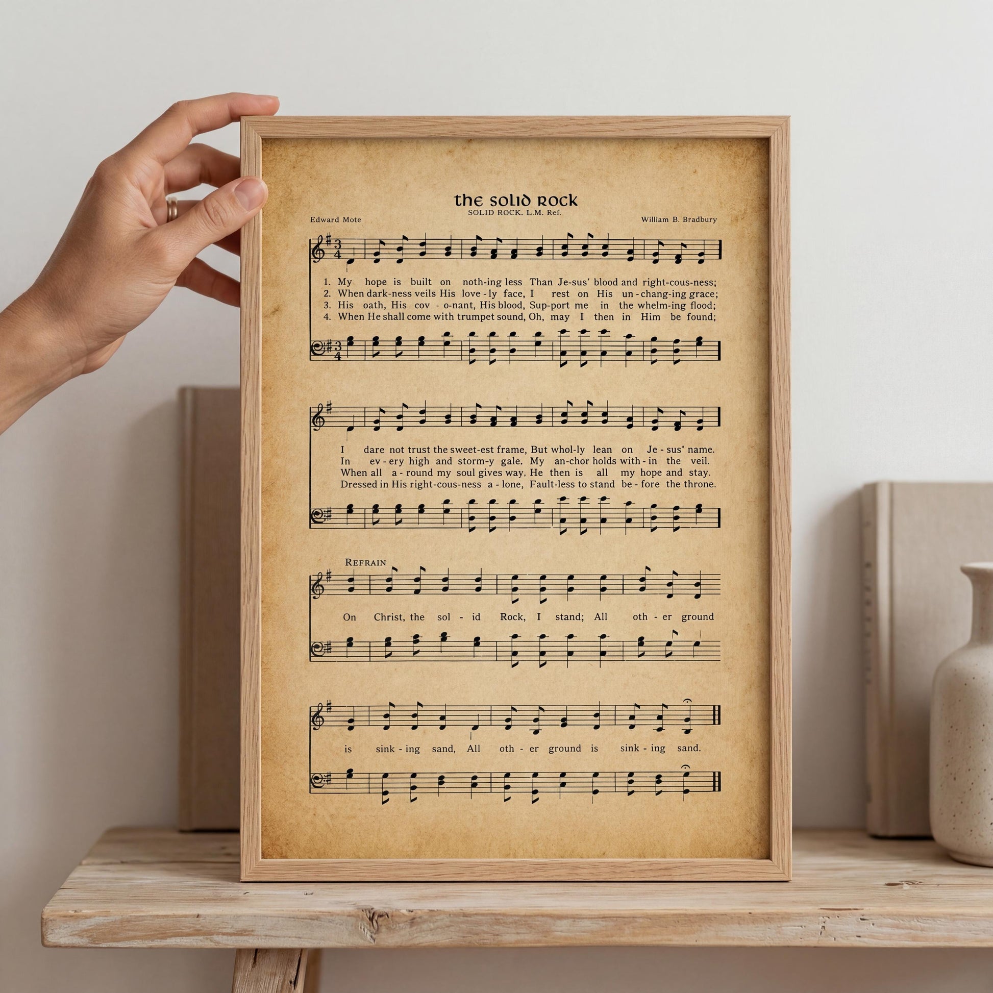 A framed sheet of music titled "The Solomons Rock" is displayed on a wooden shelf, with a hand holding it up.