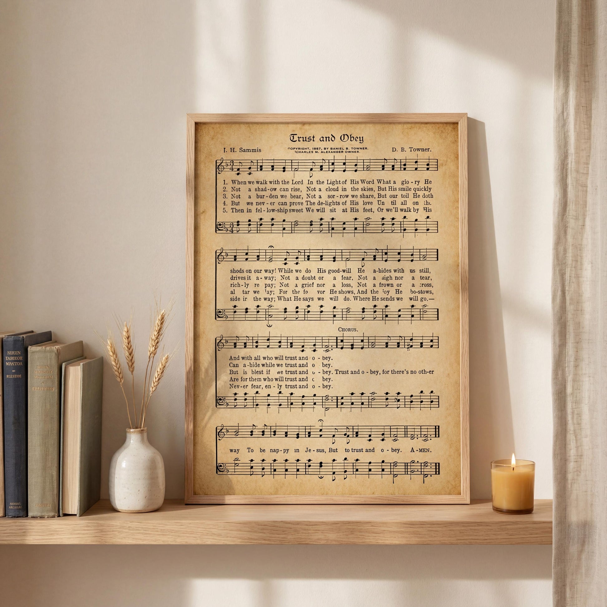 a framed sheet music poster of a hymn titled "Ent and Obej" displayed on a shelf next to a vase with wheat stalks and a lit candle.