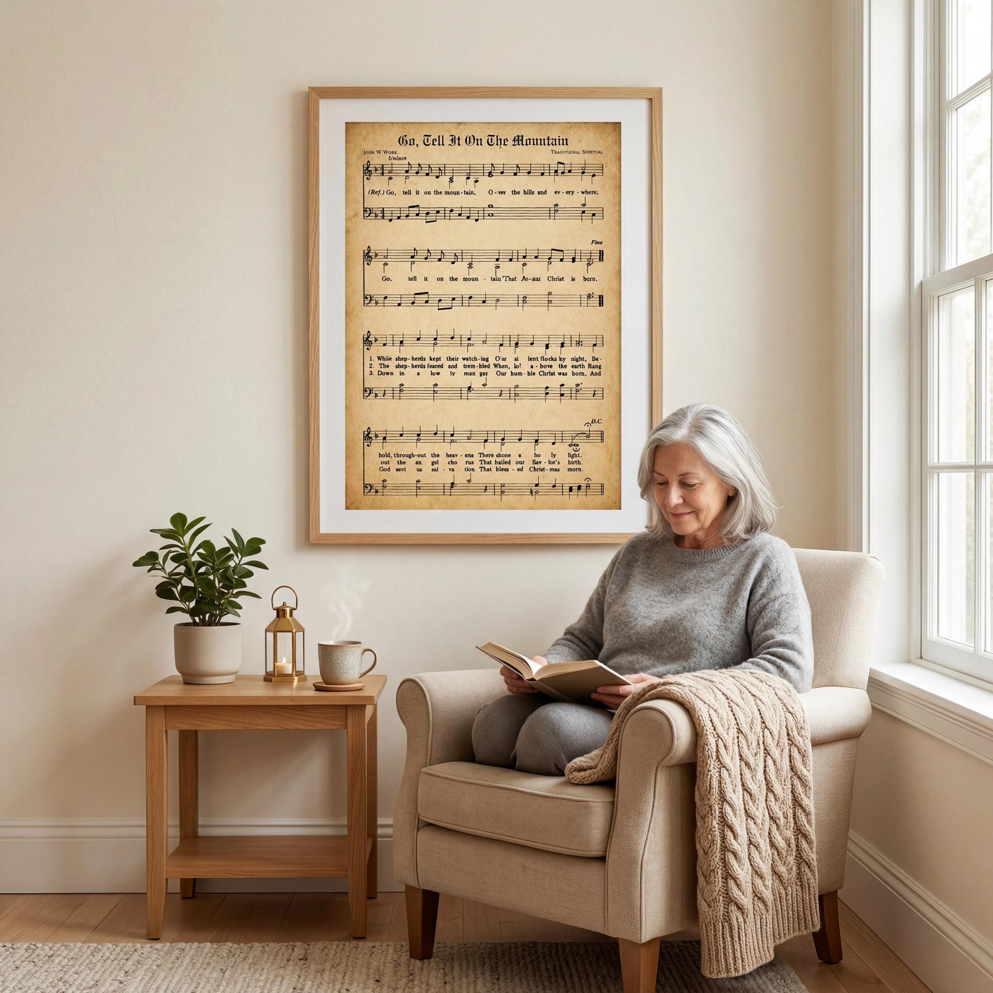 A woman is sitting in a chair, reading a book, with a framed sheet music of a song on the wall behind her.