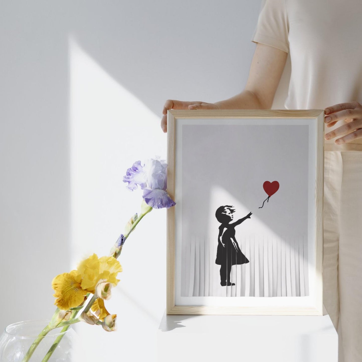 A person is holding a framed artwork featuring a silhouette of a person holding a heart-shaped balloon.
