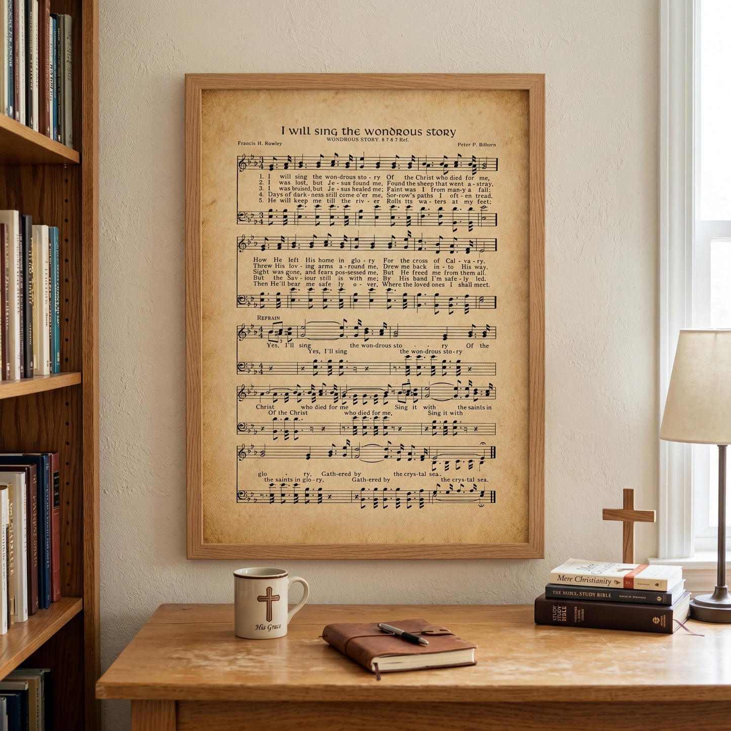 a framed sheet music poster of a hymn titled "I will sing the wonderful story" hanging on a wall above a wooden desk with a coffee mug, a book, and a cross.