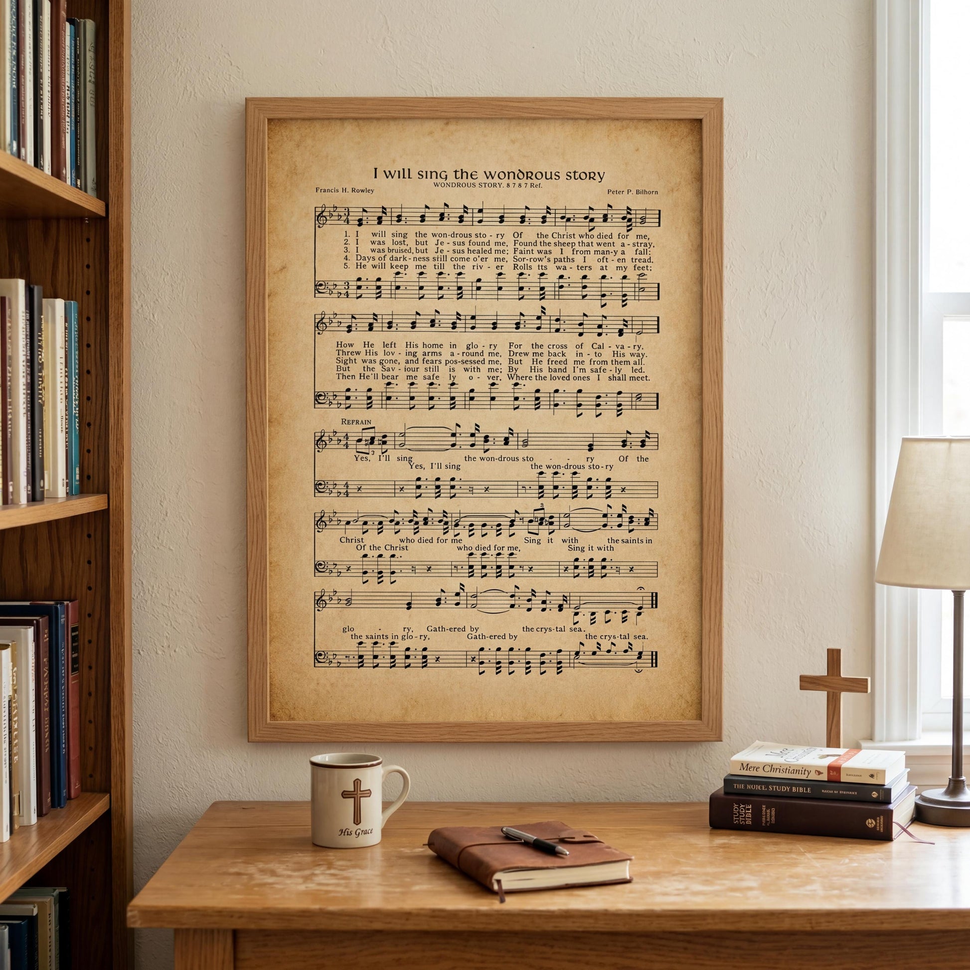 a framed sheet music poster of a hymn titled "I will sing the wonderful story" hanging on a wall above a wooden desk with a coffee mug, a book, and a cross.