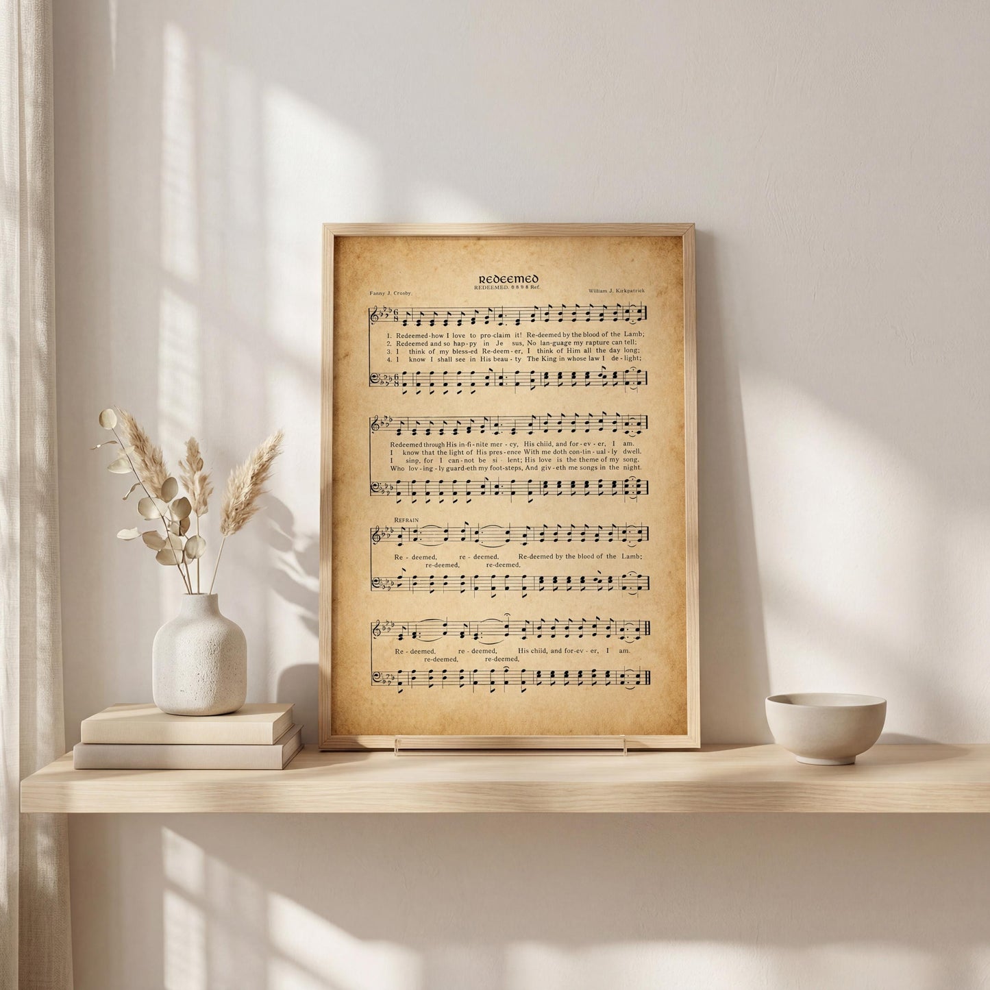 a framed sheet music print of a hymn, placed on a shelf next to a vase with dried flowers and a stack of books.