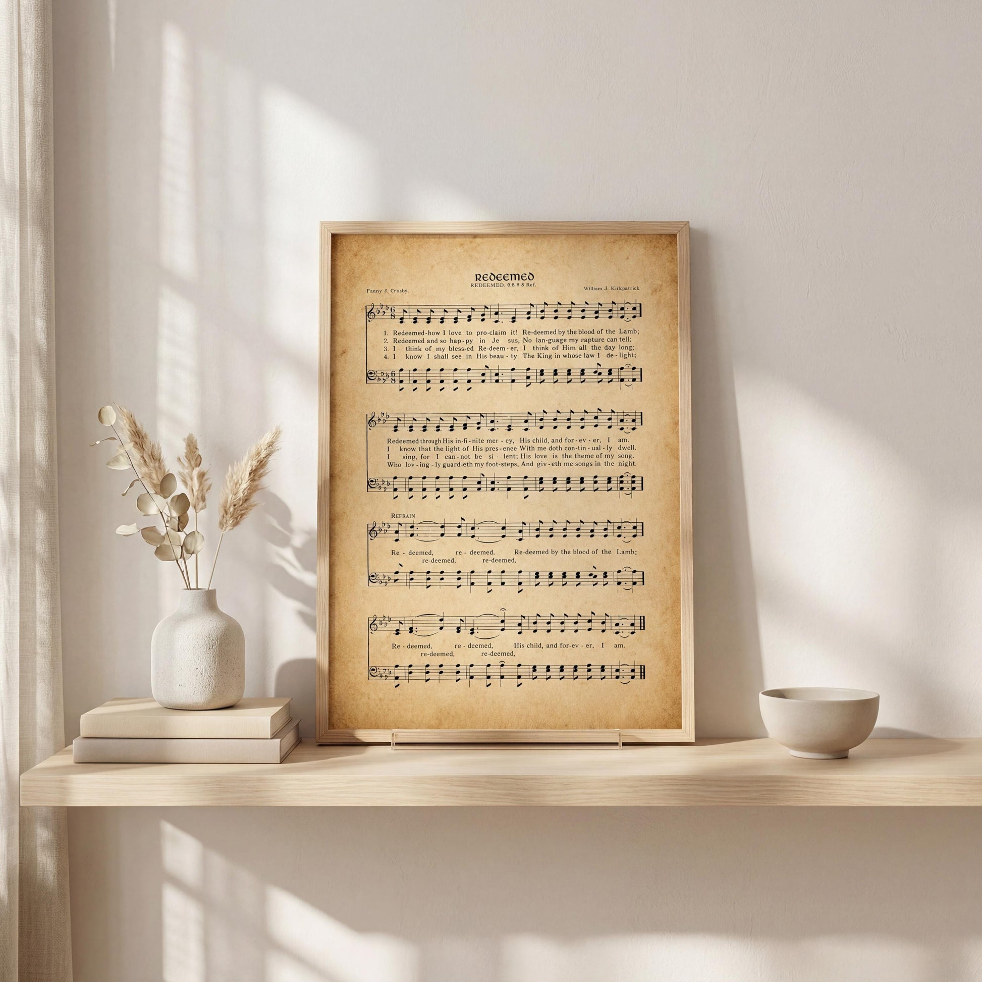 a framed sheet music print of a hymn, placed on a shelf next to a vase with dried flowers and a stack of books.