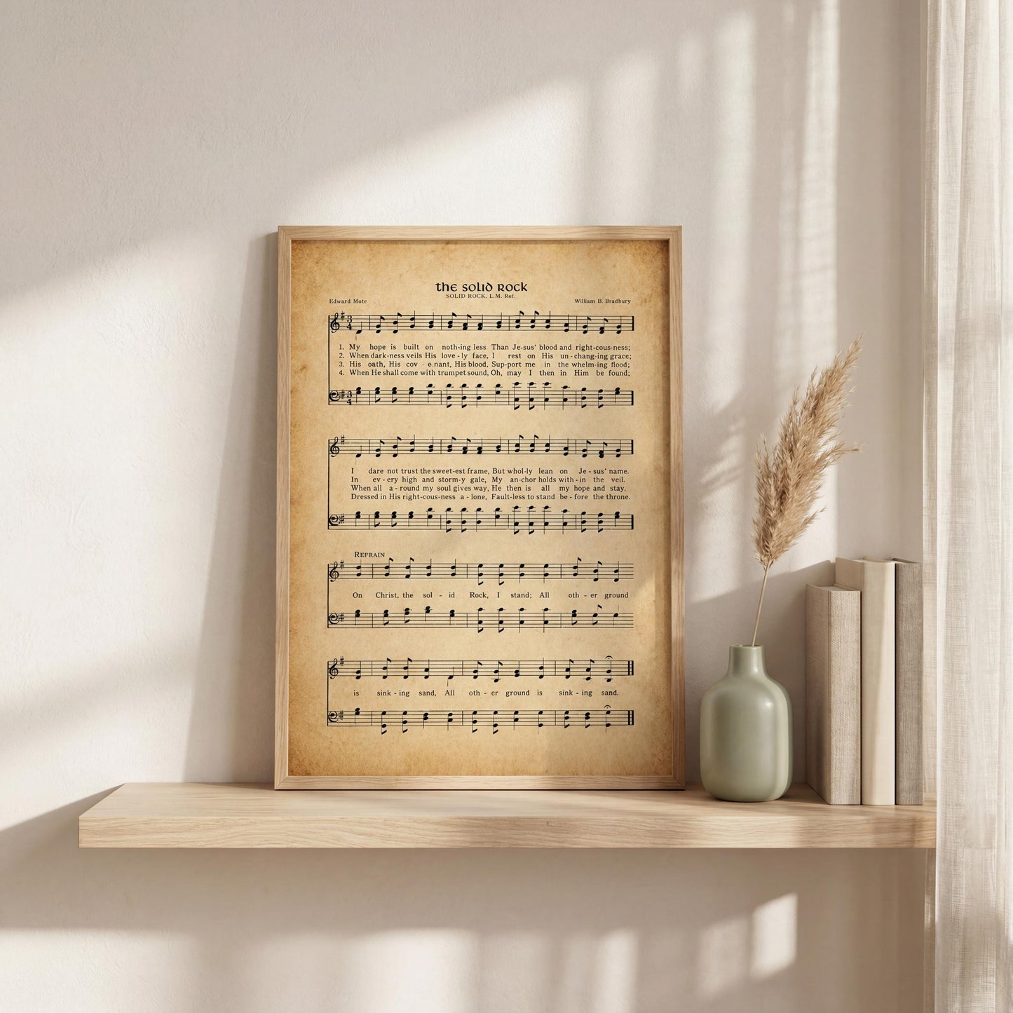a framed sheet music print of "The soliloquy" by William B. Fordham, accompanied by a vase of dried reeds and a row of books on a shelf.
