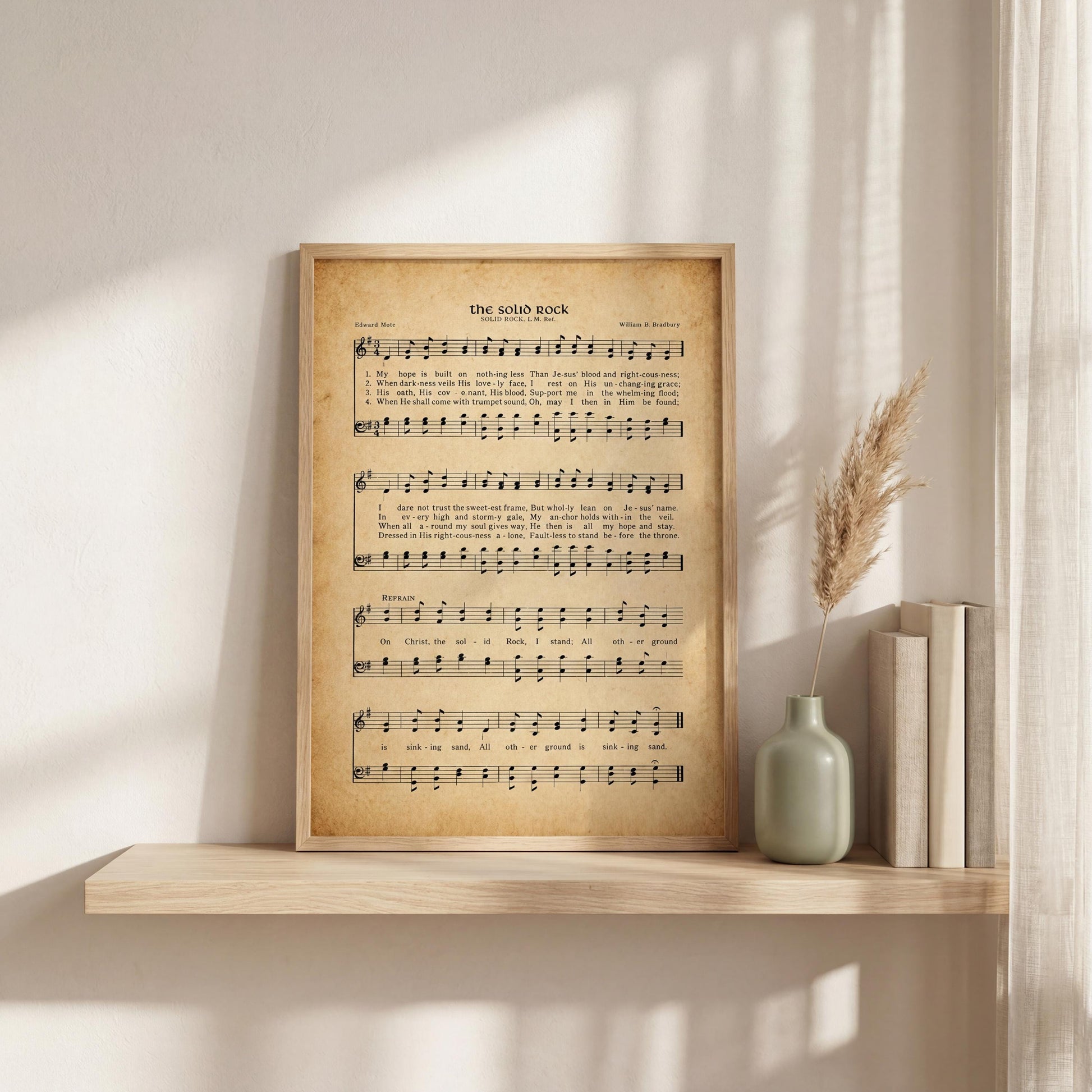 a framed sheet music print of "The soliloquy" by William B. Fordham, accompanied by a vase of dried reeds and a row of books on a shelf.