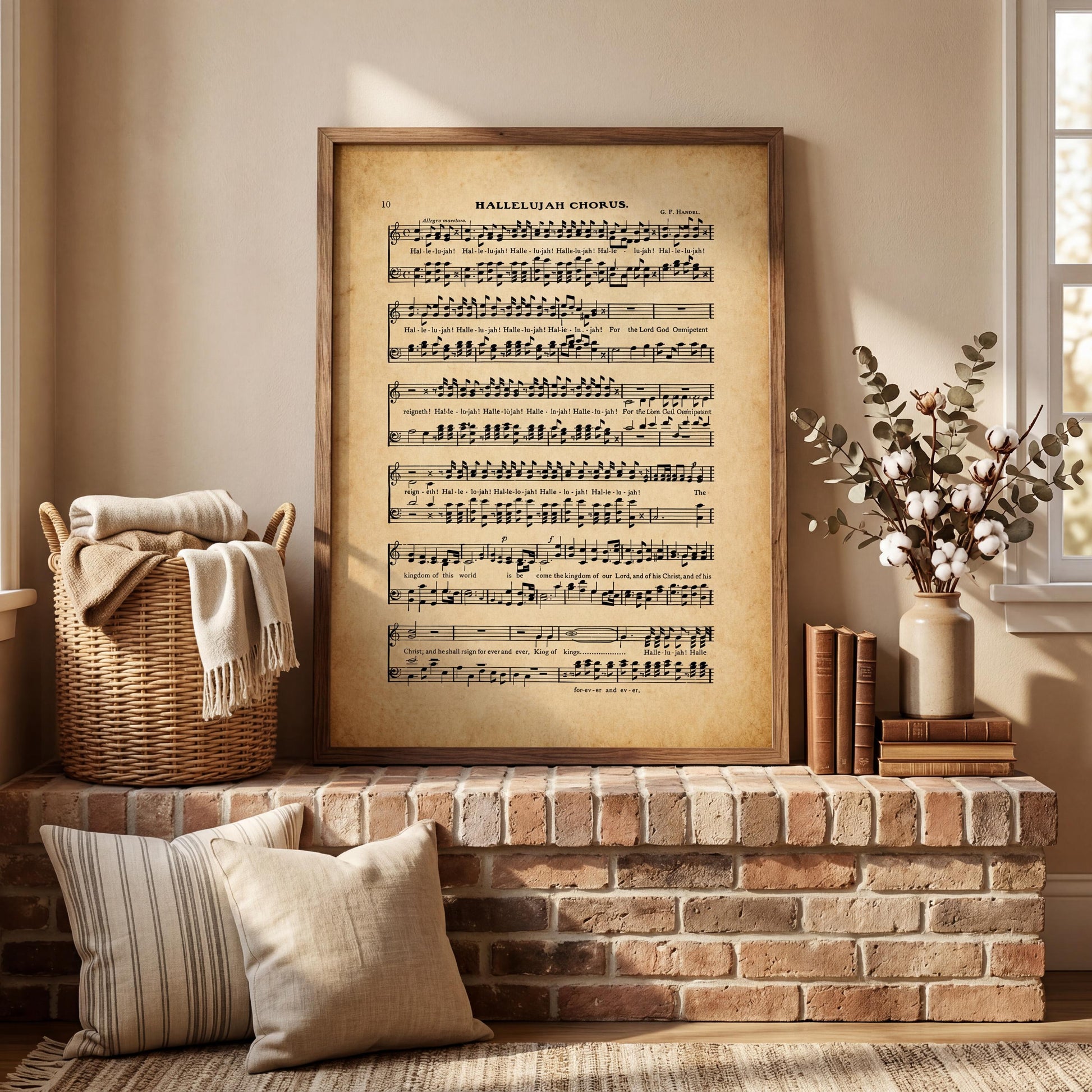 a framed sheet music print of a hymn, a wicker basket, a stack of books, and a vase of flowers on a brick fireplace mantel.