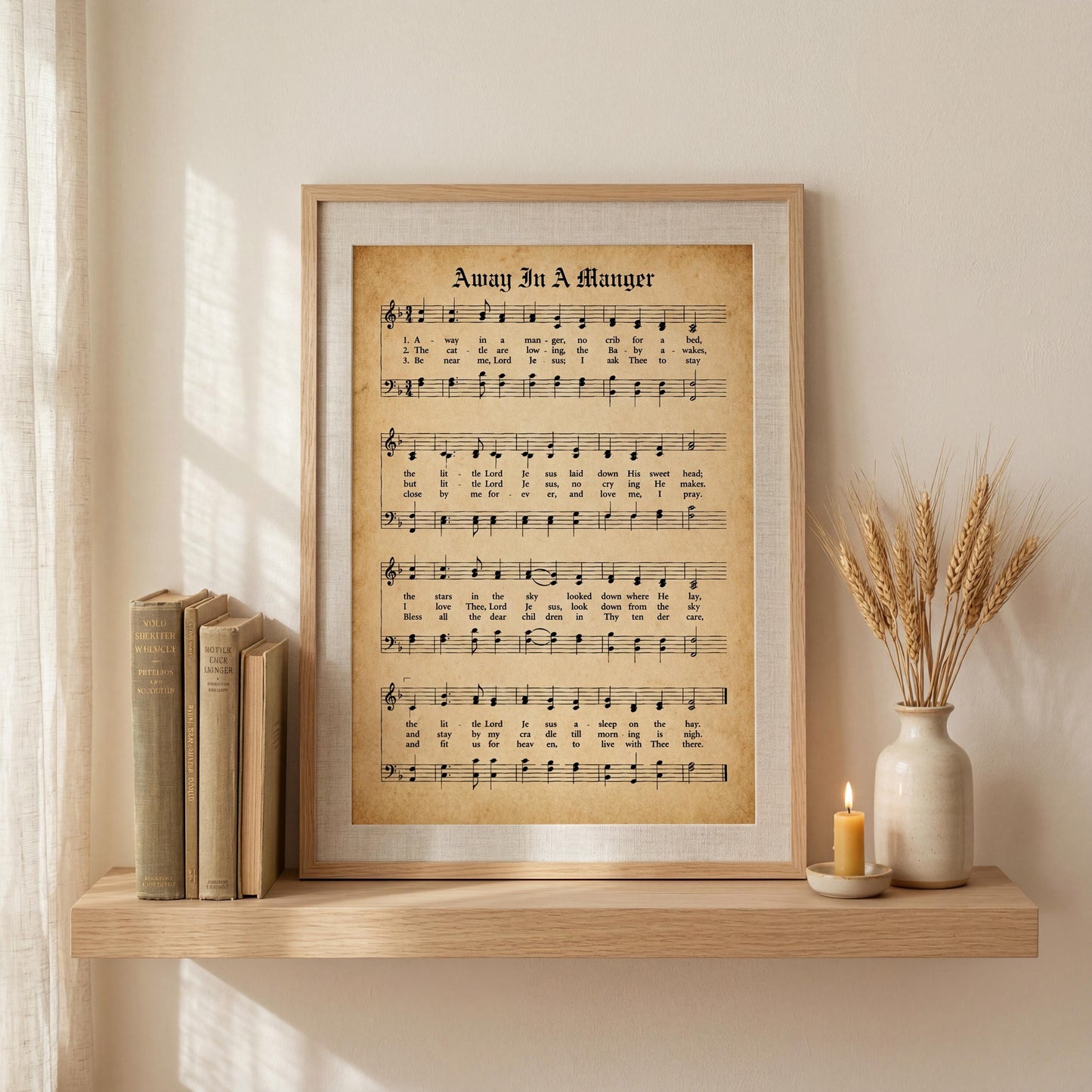 a framed sheet music print titled "Away in a Manger" displayed on a shelf, accompanied by a vase of wheat stalks and a lit candle.