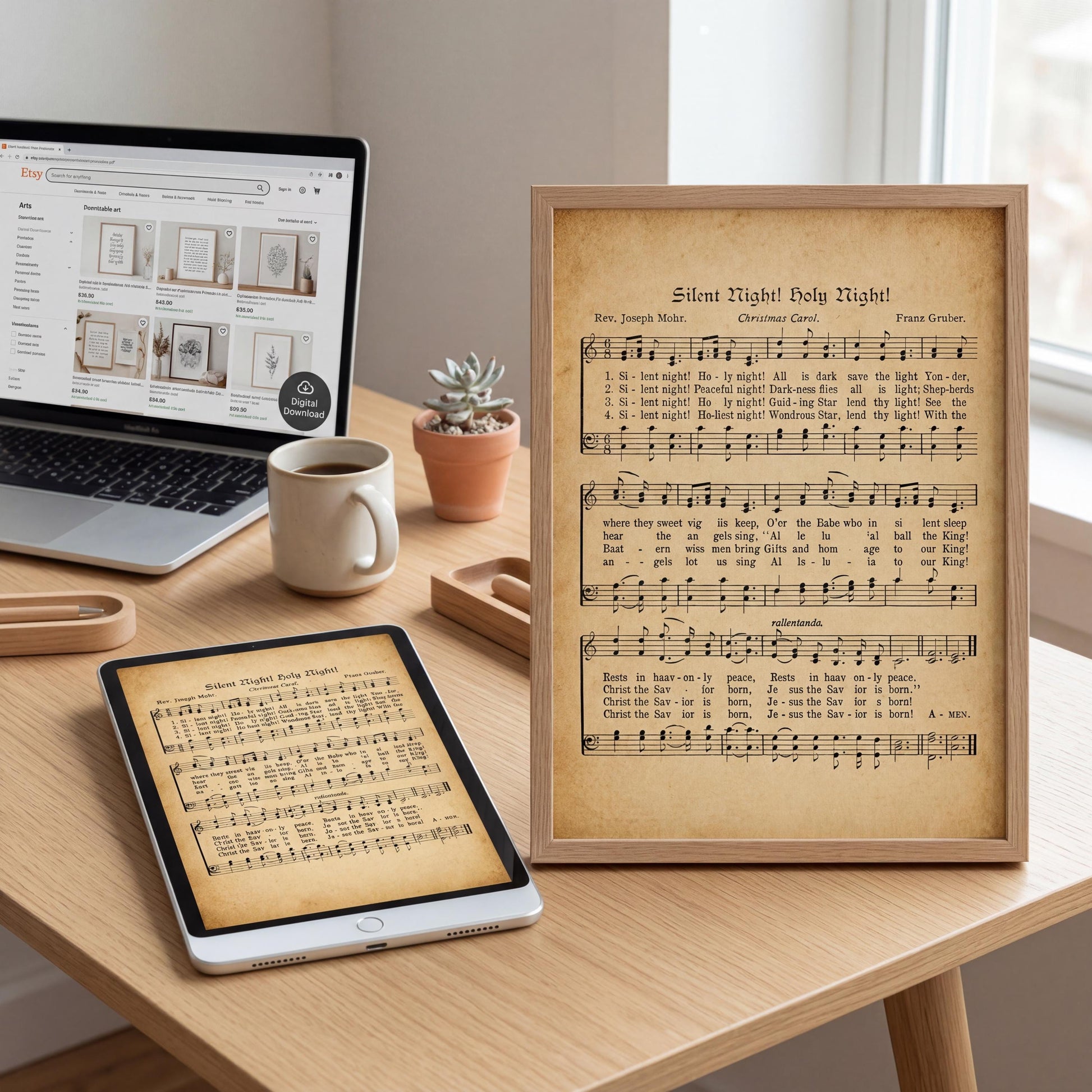 a wooden desk with a laptop, a framed sheet of music, a tablet, a coffee cup, a potted plant, and a picture frame.