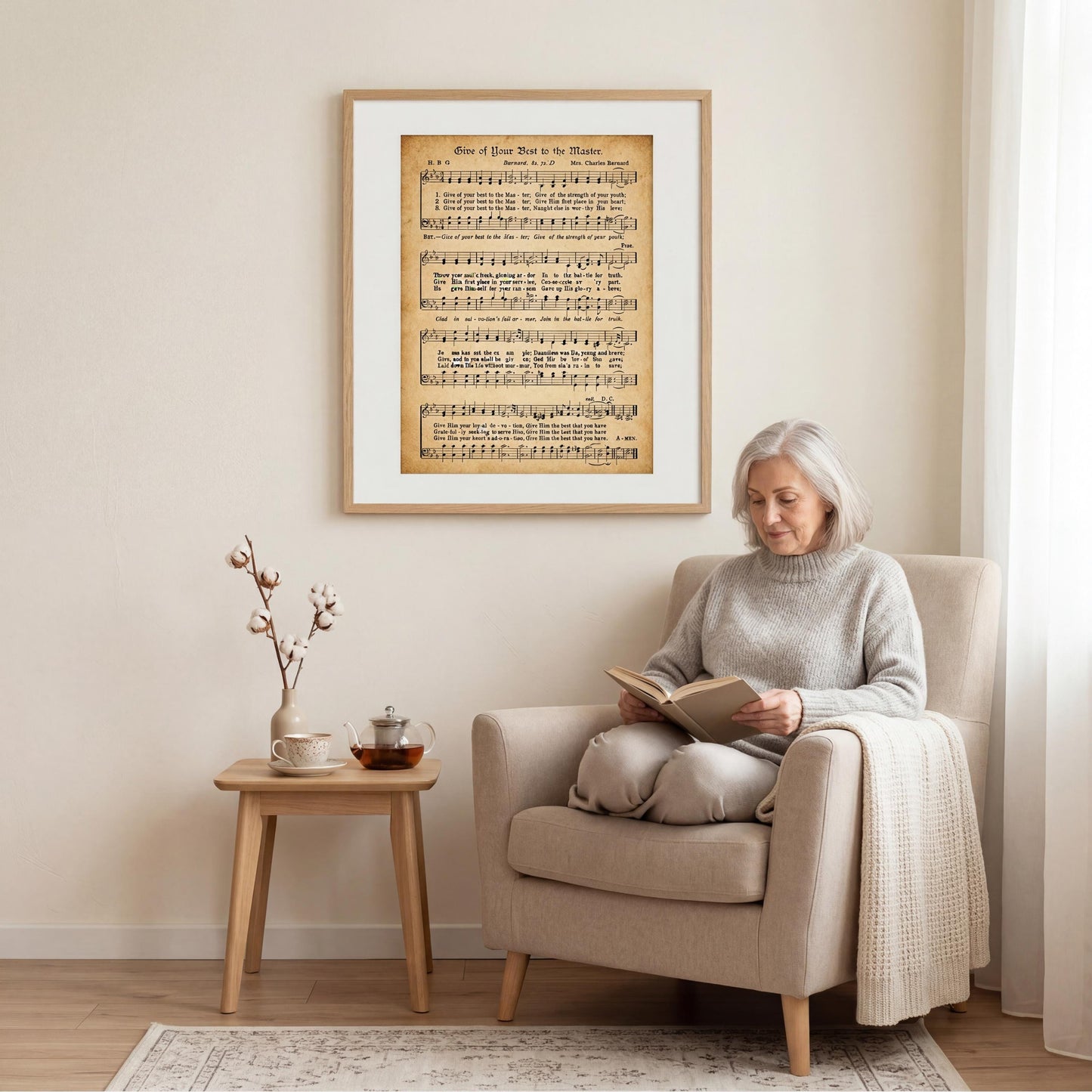 A woman is sitting in a beige armchair, reading a book, with a framed sheet music poster of a musical score hanging on the wall behind her.