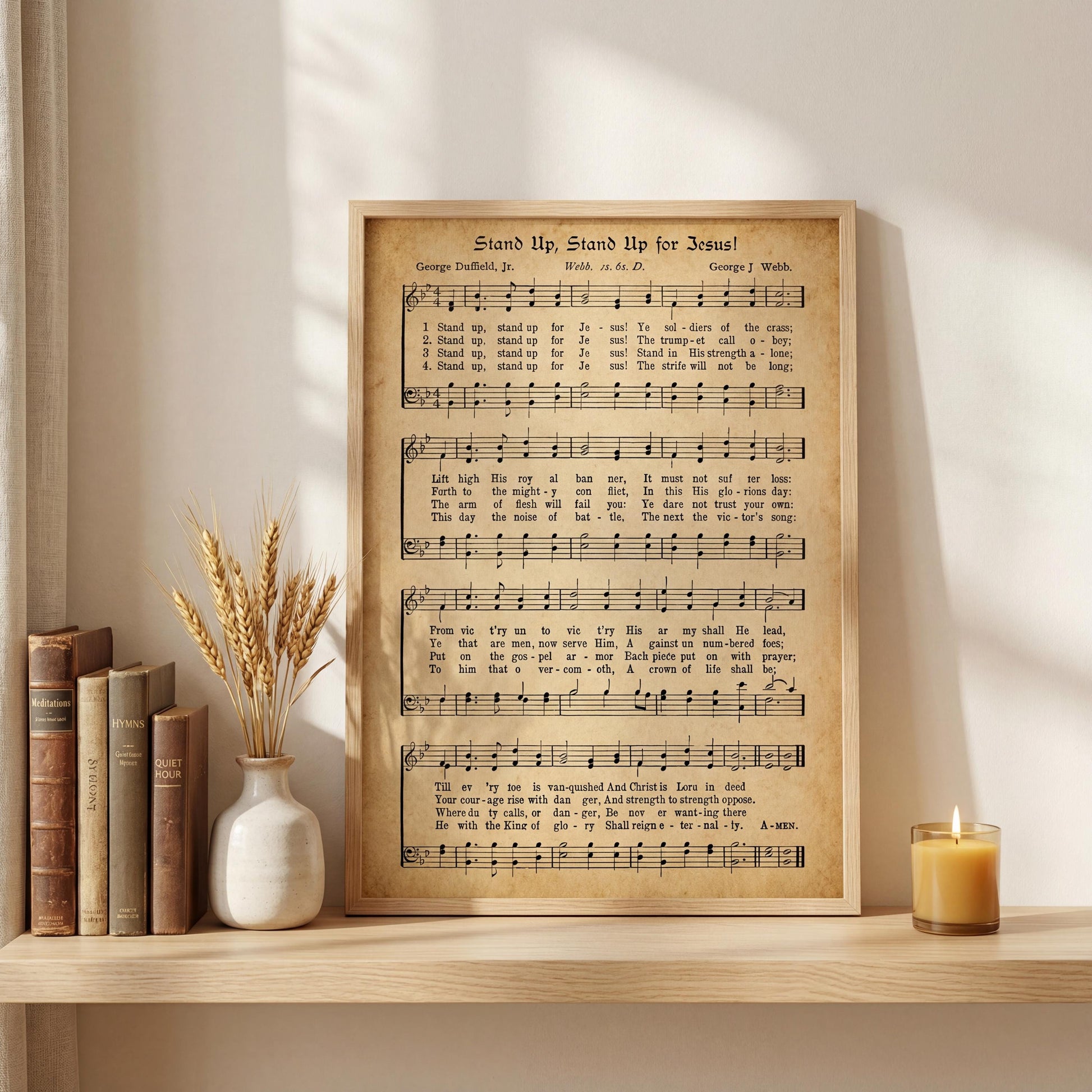 a framed sheet music poster titled "Stand Up, Stand Up for Jesus" by George David, Jr. placed on a shelf next to a vase of wheat stalks and a lit candle.
