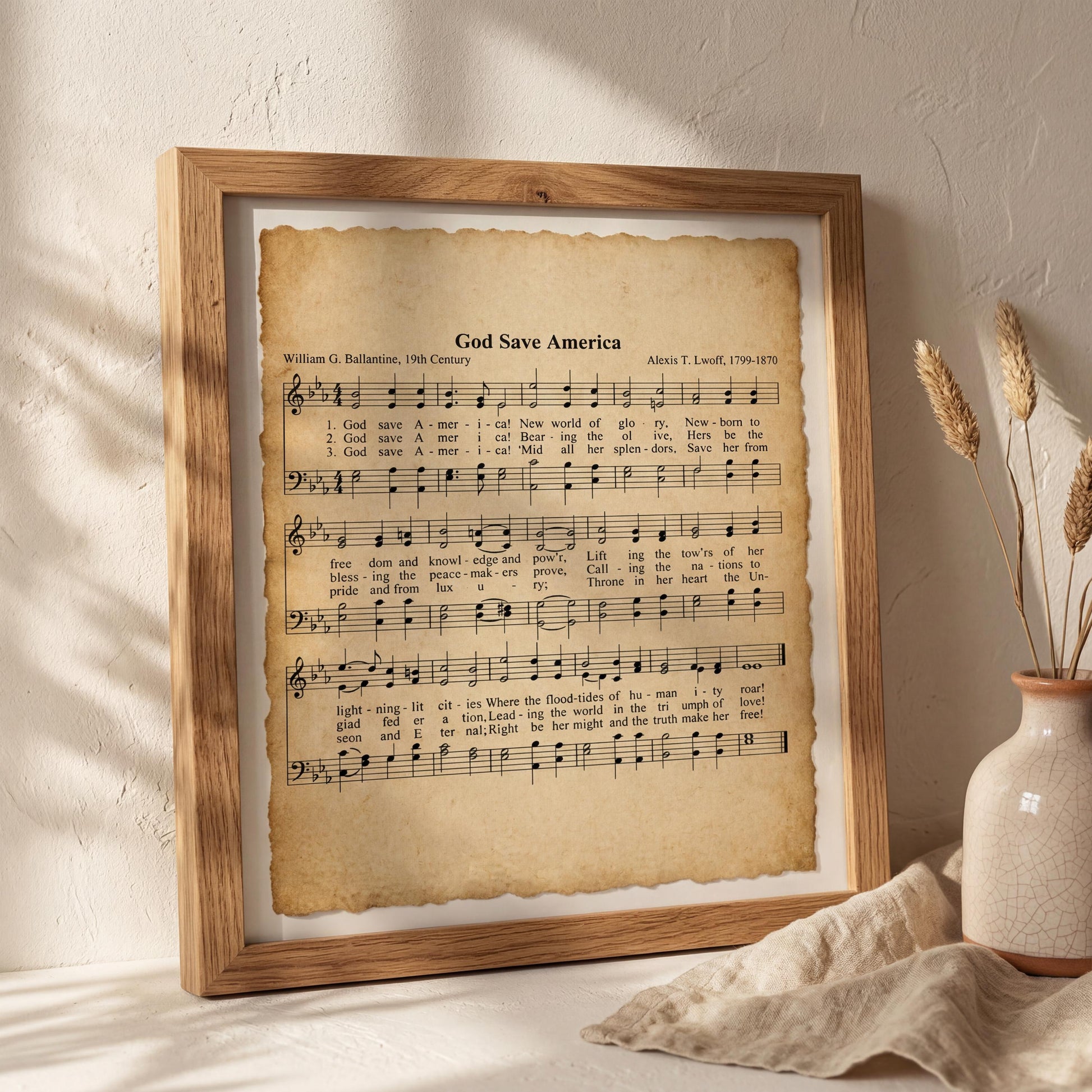 a framed sheet of music titled "God Save America" with lyrics and musical notation, placed on a white wall next to a vase with dried flowers.