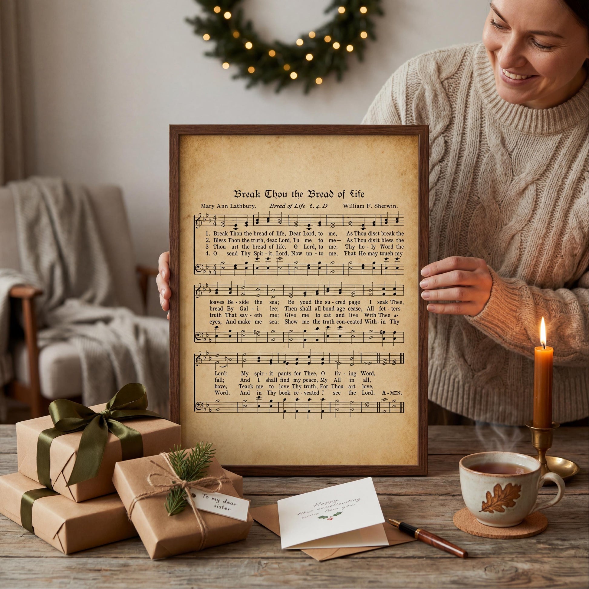 A woman is holding a framed sheet of music titled "Break Tho' the Bread of Life" in front of a lit candle, with wrapped gifts and a Christmas wreath in the background.