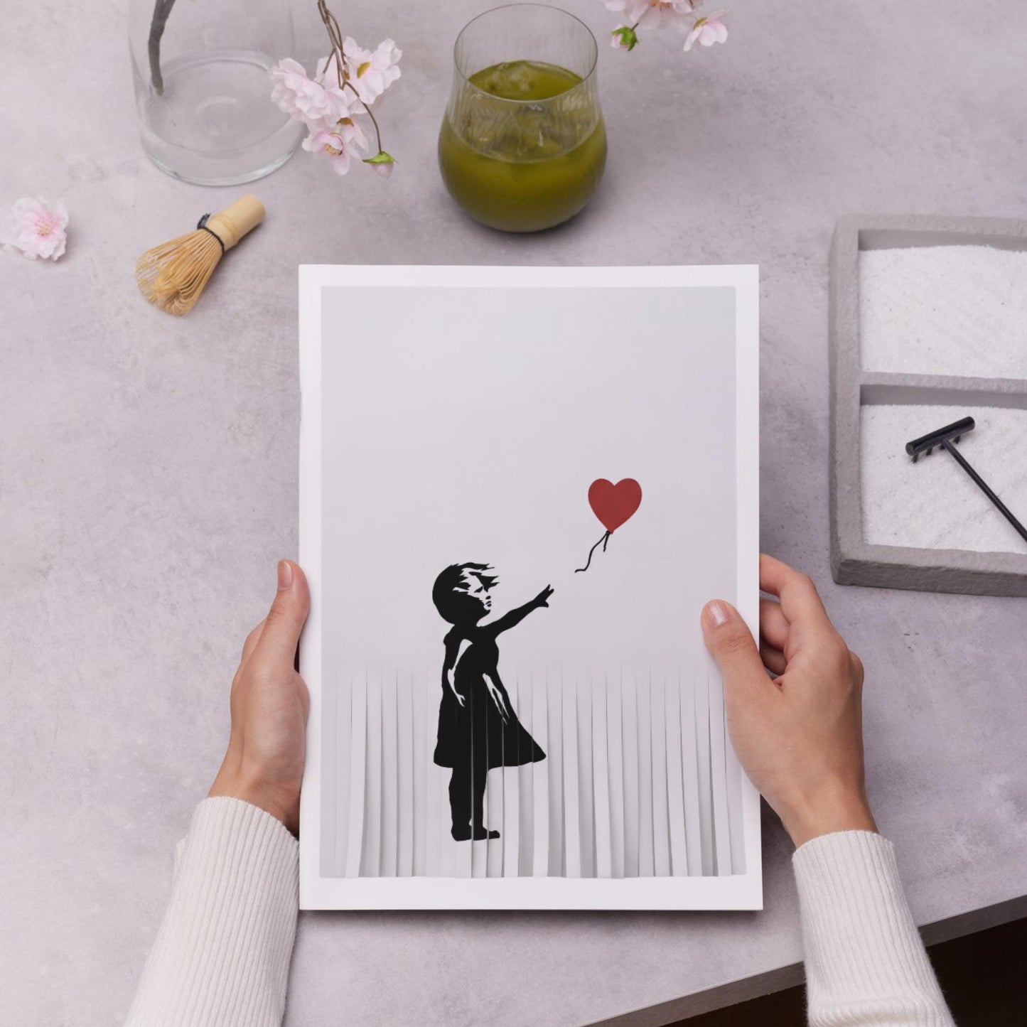 A person's hands are holding a framed print of a silhouette of a person holding a heart-shaped balloon.
