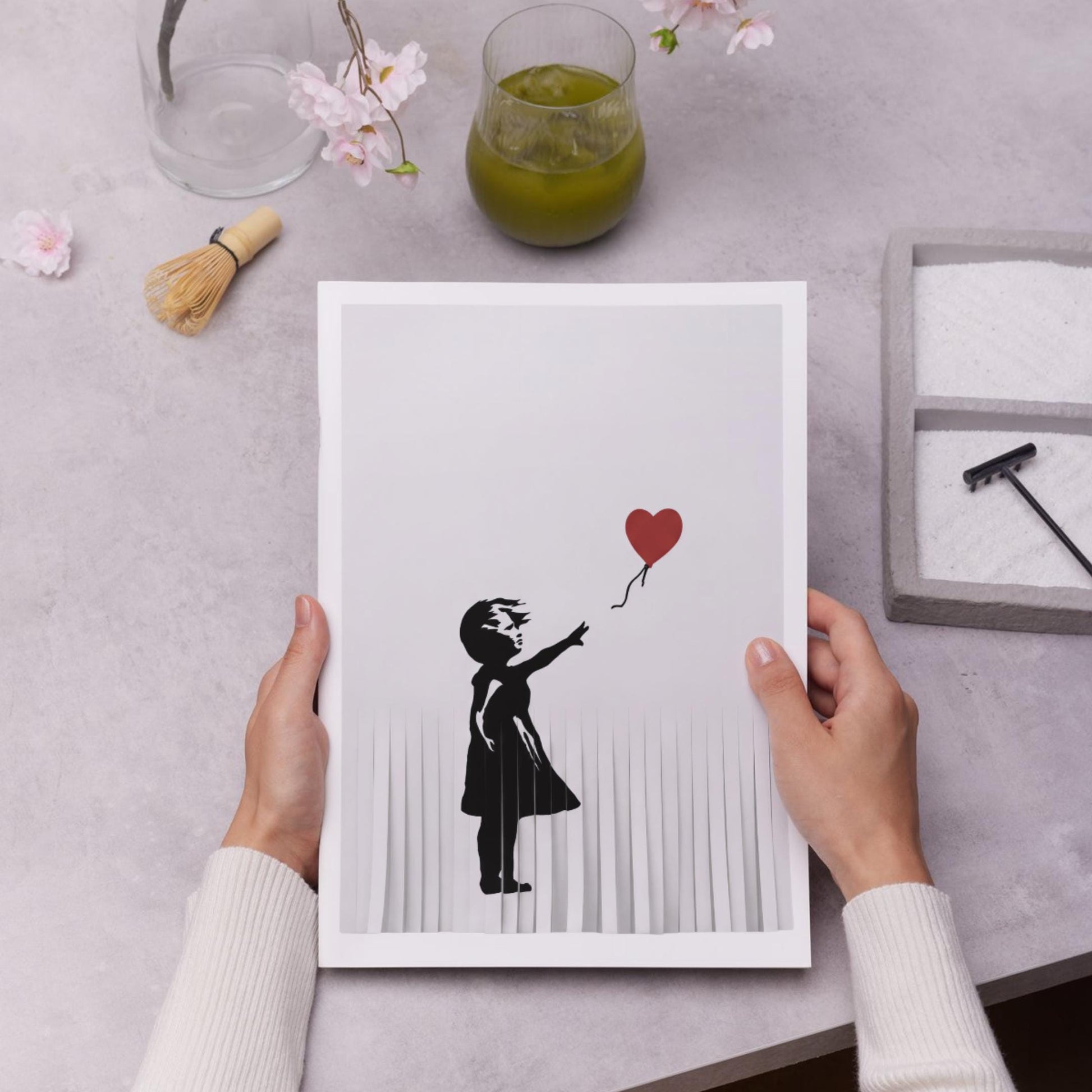 A person's hands are holding a framed print of a silhouette of a person holding a heart-shaped balloon.