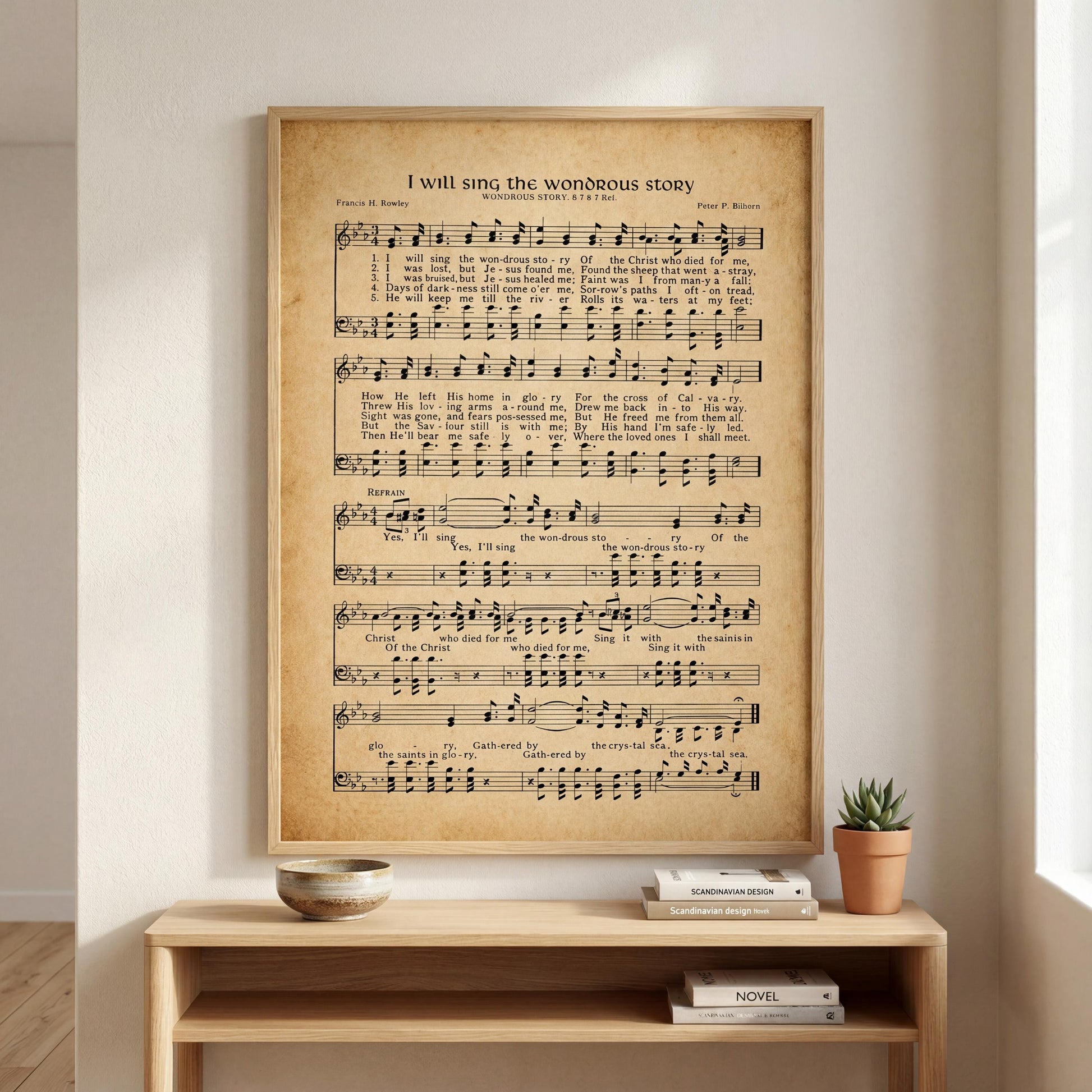 a framed sheet music poster of a hymn titled "I will sing the wonderful story" hanging on a wall above a wooden shelf with books and a small potted plant.
