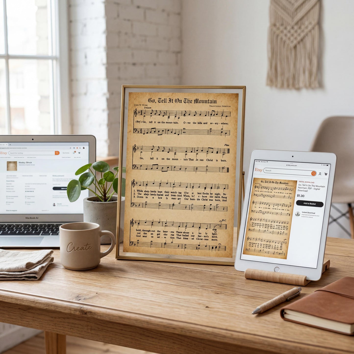 a wooden desk with a laptop, a framed sheet of music, a tablet, a coffee mug, and a plant.