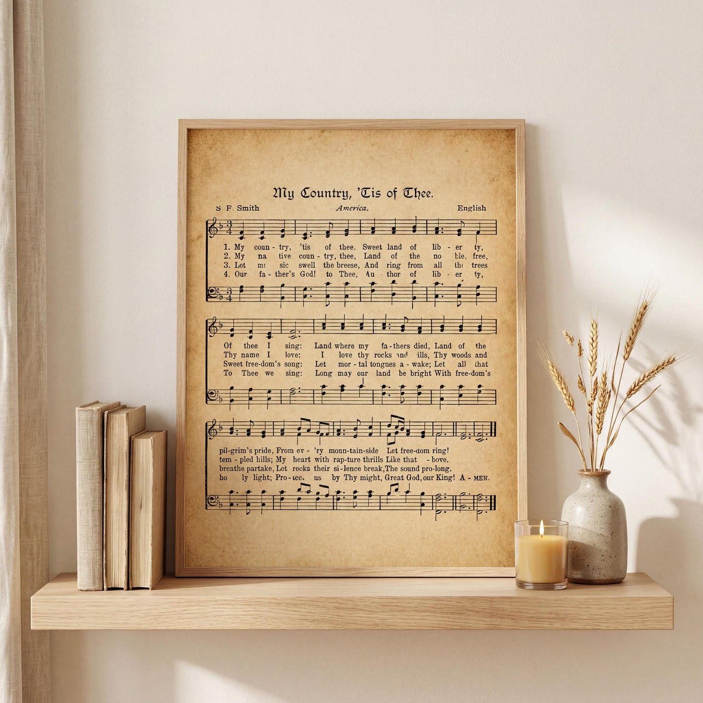 a framed sheet music poster of a hymn titled "My Country, Tis of Thee" with a wooden shelf holding several books and a vase with dried wheat stalks.