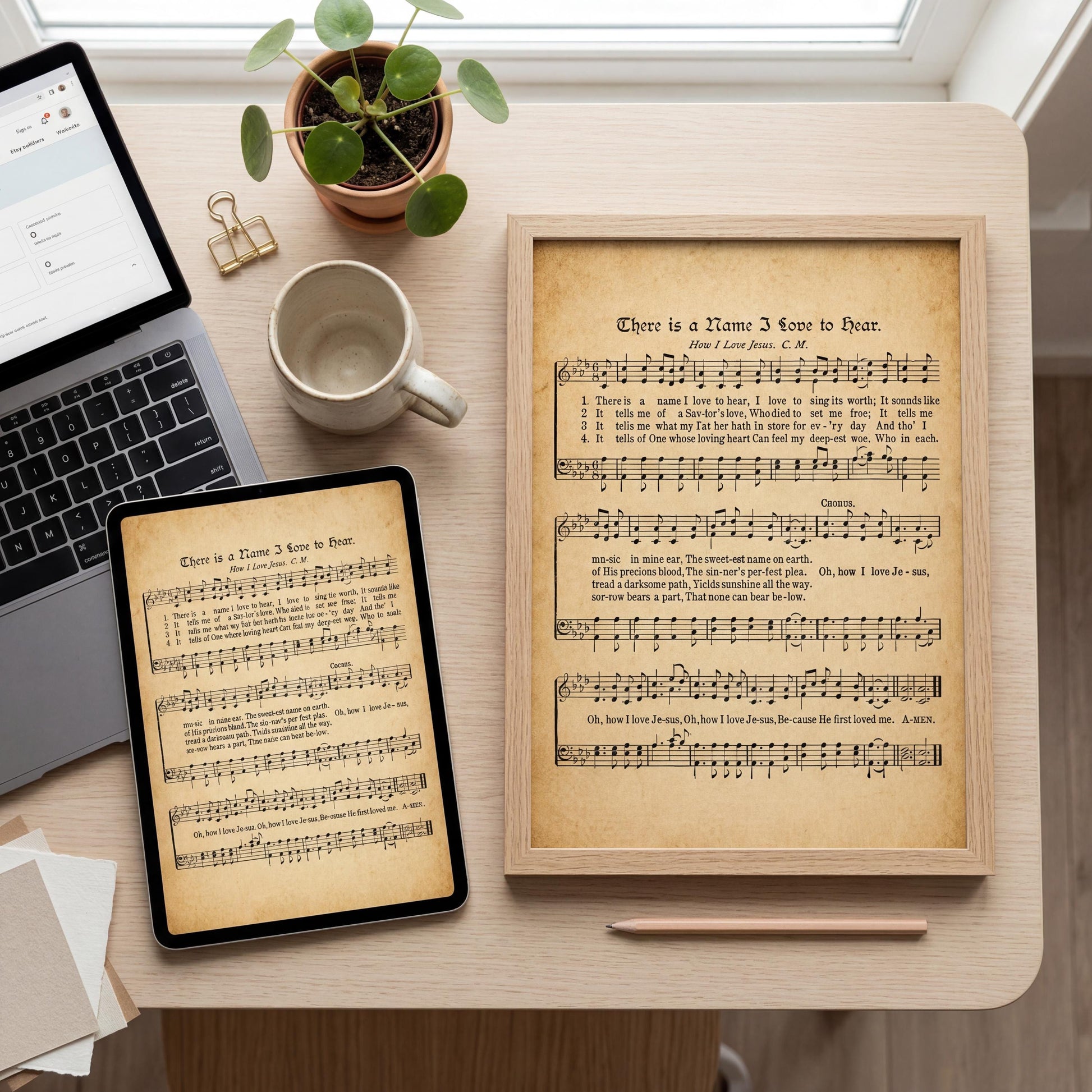 a desk with various items, including a laptop, a framed sheet of music, a cup, a potted plant, and a framed picture.