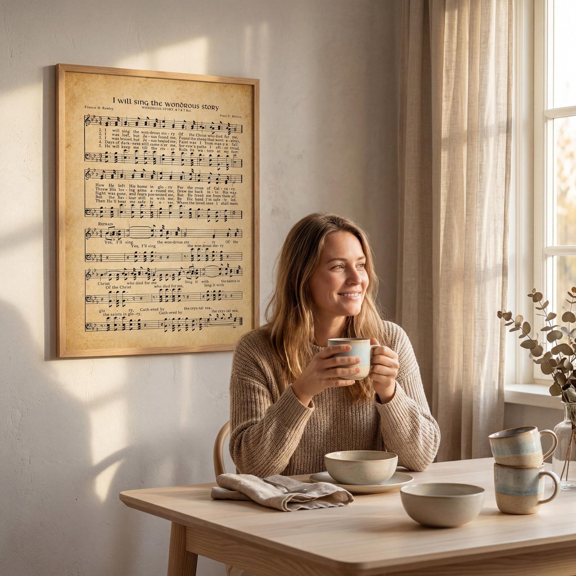 A woman is sitting at a table, holding a cup and smiling, with a framed sheet music poster on the wall behind her.