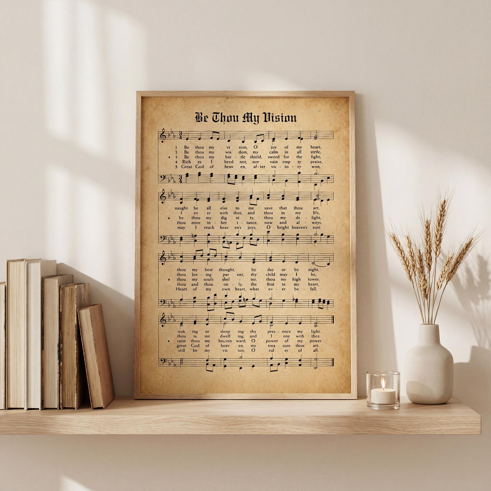 a framed sheet music poster titled "Be Thou My Vision" displayed on a shelf next to a vase with wheat stalks.