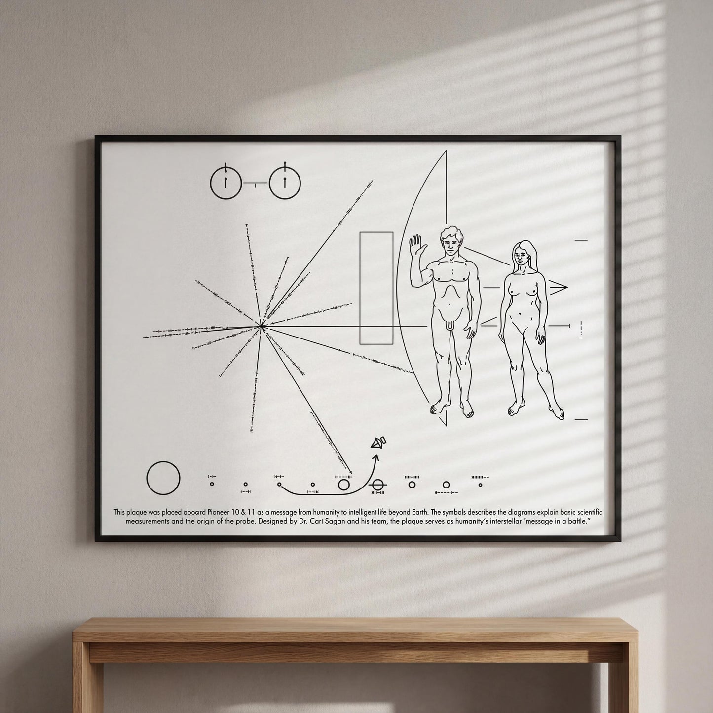 The image is a framed artwork depicting a black and white line drawing of a spacecraft with two figures, one male and one female, standing in front of a large planet. The artwork is described as a message from harmony to the Earth, and it is placed on a wall above a wooden table.